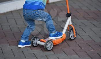 Boy child in blue jeans and sneakers riding a scooter.