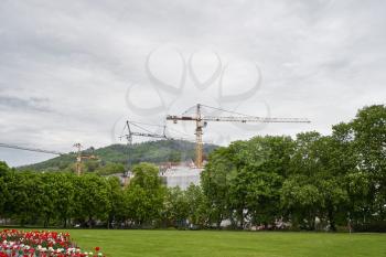 Construction cranes are building near the city park in the European city
