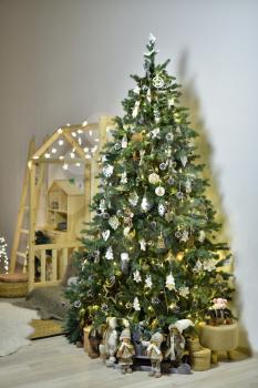 A large Christmas tree decorated with toys and gnomes in a children's playroom with wooden furniture, a house decorated for the New Year or Christmas.