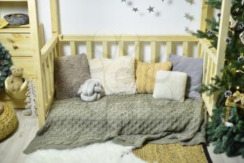 Children's playroom with wooden furniture, a house with soft pillows, decorated for the New Year or Christmas.
