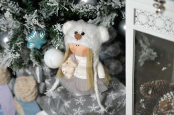Children's cute stuffed doll stands next to the Christmas tree.