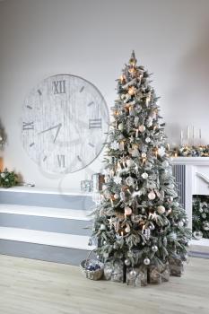 Christmas light interior with a snow-covered Christmas tree by the fireplace and a large wall clock.