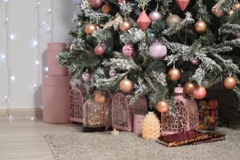 Decor in the form of lamps stands under a beautiful snow-covered and decorated with balls Christmas tree