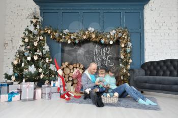 Family dad mom and daughter sit on the carpet and have fun on the background of Christmas decor, chalk inscription happy new year, Christmas tree and gifts