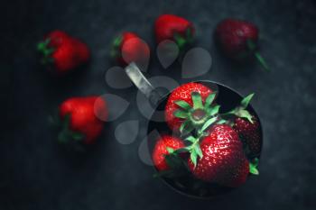 Ripe strawberries scattered around an iron mug