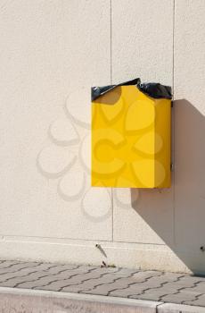 Royalty Free Photo of a Yellow Garbage Can Hanging on Wall at a Sidewalk
