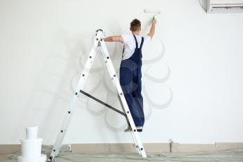 Male painter using roller for refurbishing color of wall indoors�