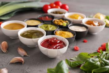 Different tasty sauces in bowls on grey table�
