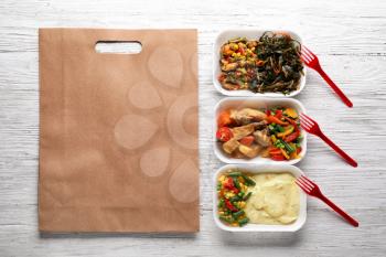 Plastic containers with delicious food and paper bag on wooden table. Delivery service�