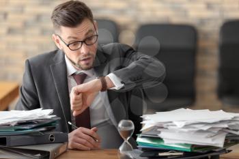 Businessman looking at his wristwatch at table in office. Time management concept�