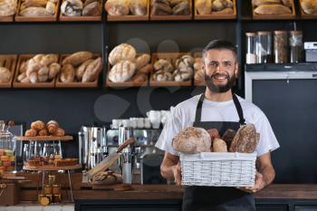 Male baker holding wicker basket with fresh bread in shop�
