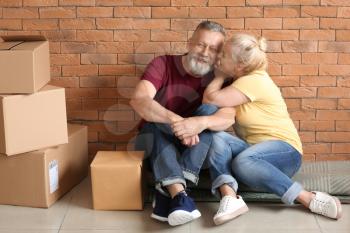 Happy mature couple with moving boxes sitting on carpet at new home�
