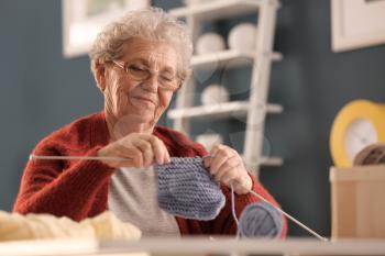 Senior woman knitting warm sock at home�