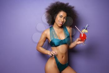 Beautiful African-American woman in bikini and with tasty cocktail on color background�