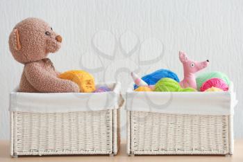 Wicker baskets with balls of knitting yarn and funny toys on table against light background�