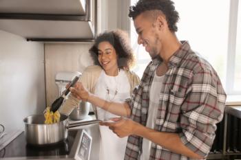 Young African-American couple cooking together in kitchen�