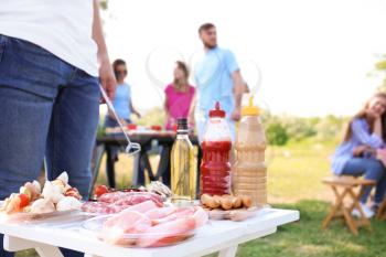 Table with raw products for barbecue and company of friends outdoors�
