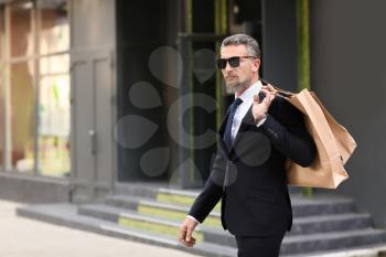 Handsome mature man in suit with shopping bags near store outdoors�