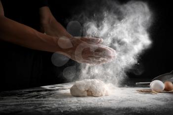 Man clapping hands and sprinkling flour over dough on black background�