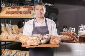 Man holding board with assortment of fresh bread in bakery�