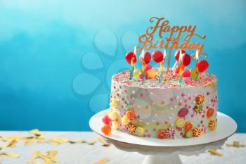Stand with beautiful tasty birthday cake on table against color background�