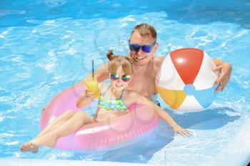 Happy father and daughter with inflatable ring and ball in swimming pool�