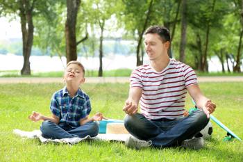 Little boy and his father practicing yoga outdoors�