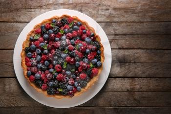 Plate with delicious berry pie on wooden background, top view�