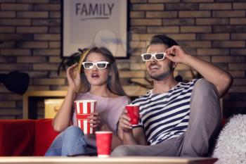 Young couple in 3d glasses watching movie on sofa at night�