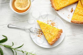 Plate with piece of tasty lemon pie and cup of tea on white wooden table�