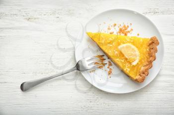 Plate with piece of tasty lemon pie on white wooden table�