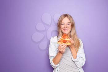 Young woman eating slice of delicious pizza on color background�