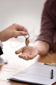 Real estate agent giving key of new house to man in office�