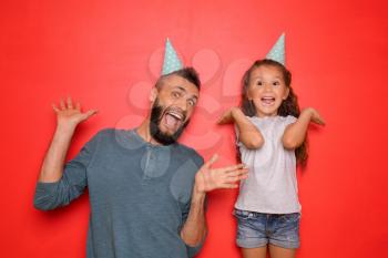 Funny portrait of father and his little daughter with party hats on color background�
