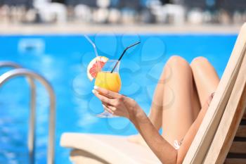 Beautiful young woman with cocktail resting on sun lounger at resort�