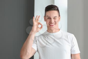 Handsome young man in casual clothes showing OK gesture near window�