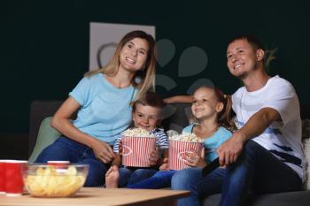 Happy family watching TV and eating popcorn in evening�
