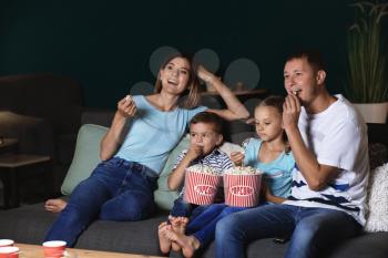 Happy family eating popcorn while watching TV in evening�