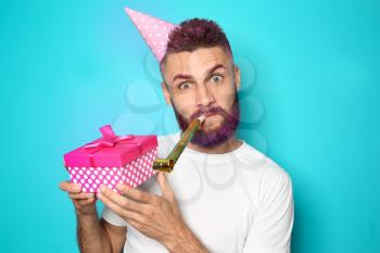 Funny portrait of man with Birthday gift and party whistle on color background�