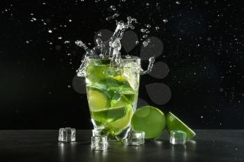 Glass of fresh mojito with splashes on dark background�