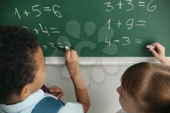 Schoolchildren writing on chalkboard in classroom during math lesson�