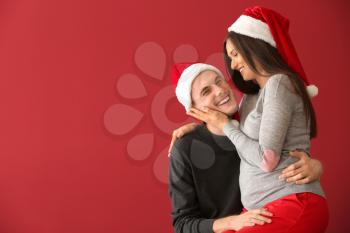 Portrait of cute young couple in Santa hats on color background�