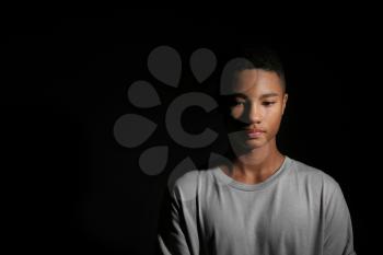 Sad African-American teenage boy on dark background�