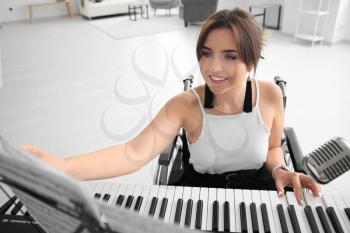 Beautiful young musician in wheelchair playing synthesizer at home�