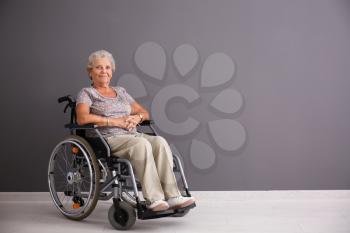 Senior woman in wheelchair near grey wall�
