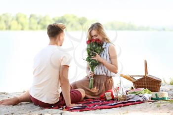 Young woman receiving flowers from her boyfriend on romantic date near river�