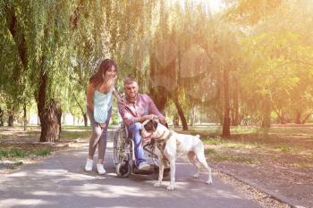Young man in wheelchair with his wife and service dog outdoors�