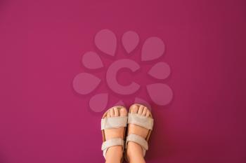 Legs of girl wearing sandals on color background�