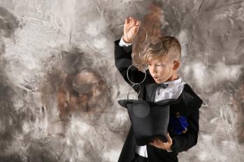 Cute little magician showing trick with hat on grunge background�