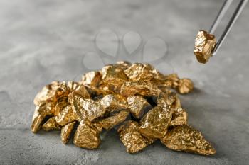 Taking of gold nugget with pincer from grey table�